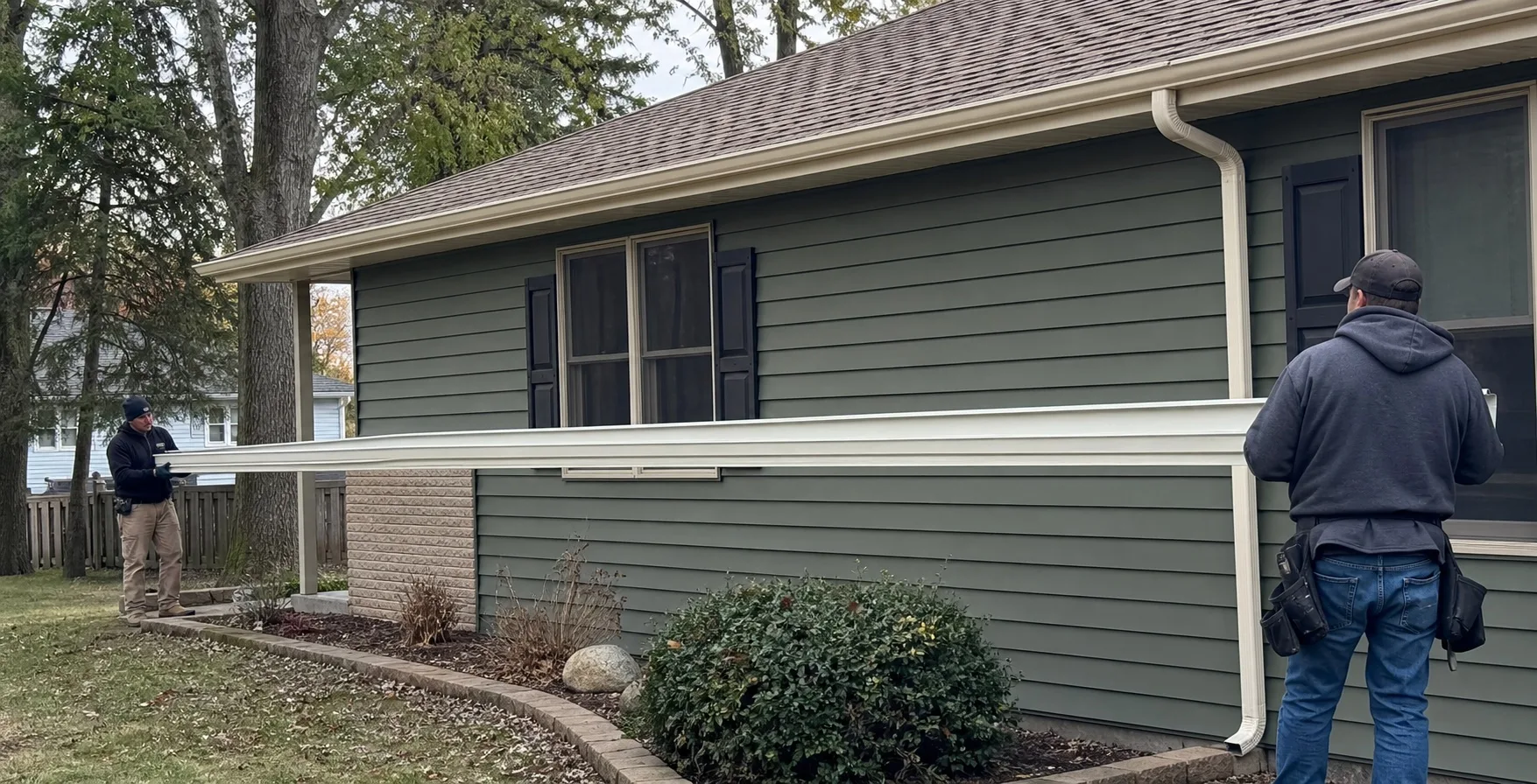 Two gutter professionals carrying one long continuous aluminum gutter section